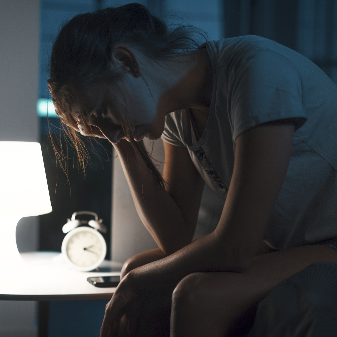 Erschöpfte Frau sitzt nachts wach im Bett – Sinnbild für Schlafmangel, Müdigkeit und eingeschränkte Regeneration.